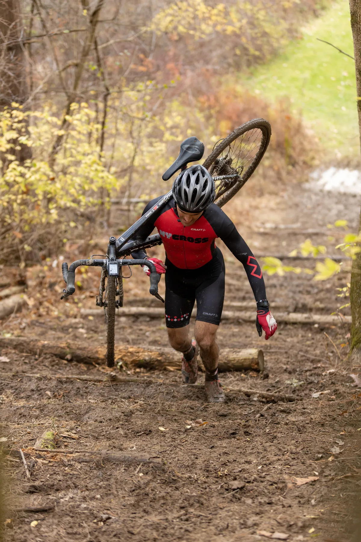 Cyclocross racer shouldering his bike up a muddy wooded run-up