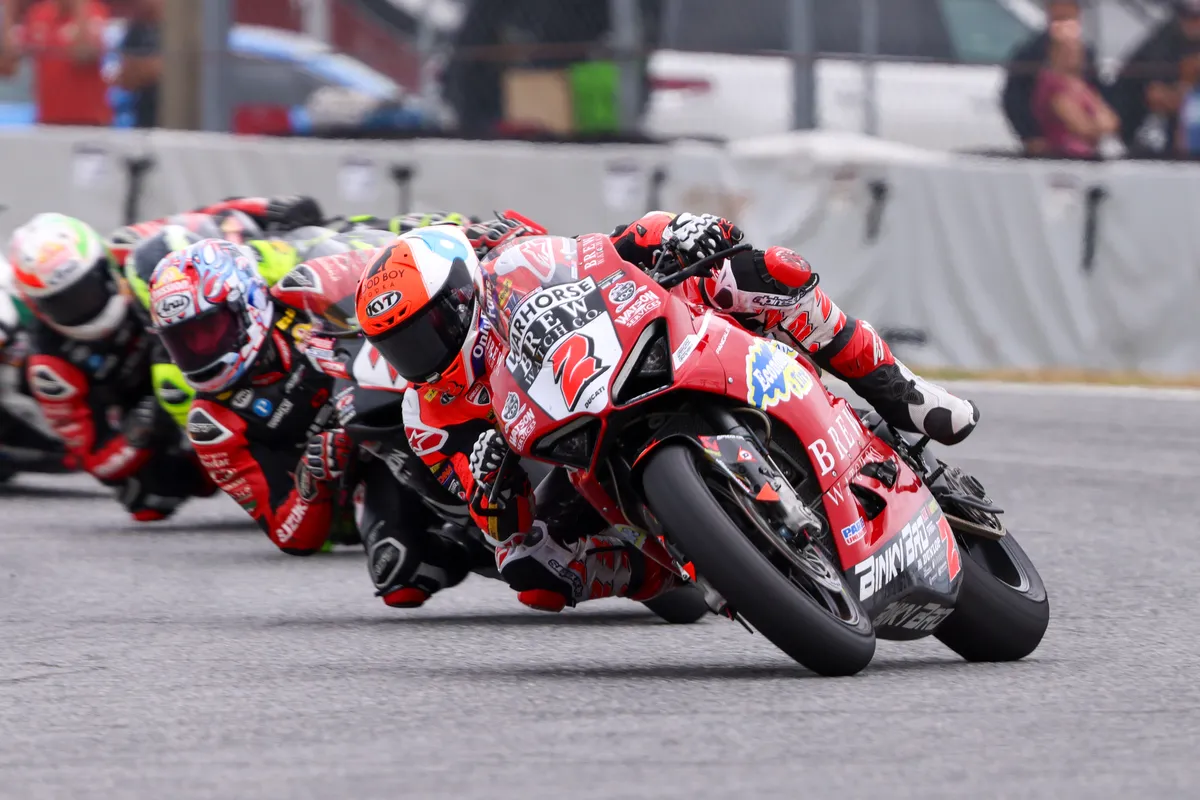 Road racer leading a pack through a corner, knee down on a red Ducati at Daytona