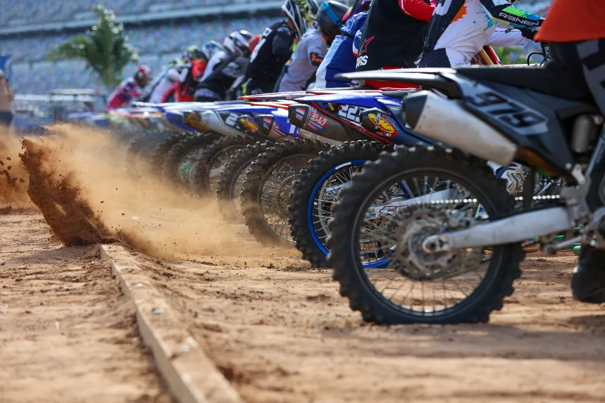 Row of motocross bikes spraying dirt as the start gate drops