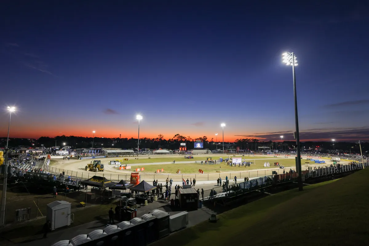 Daytona flat track oval glowing under the lights against an orange sunset sky