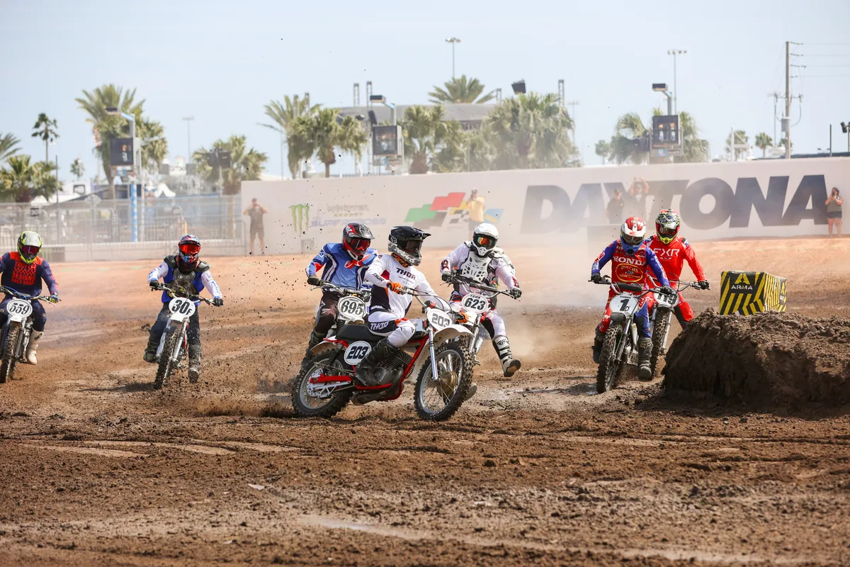Vintage motocross riders charging out of the first turn with the Daytona banner behind