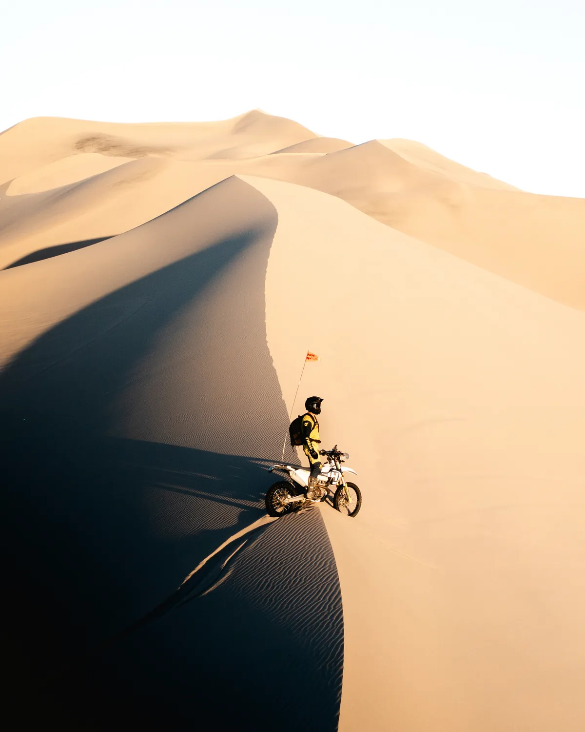 Dirt bike rider on a sweeping dune ridge at Dumont Dunes