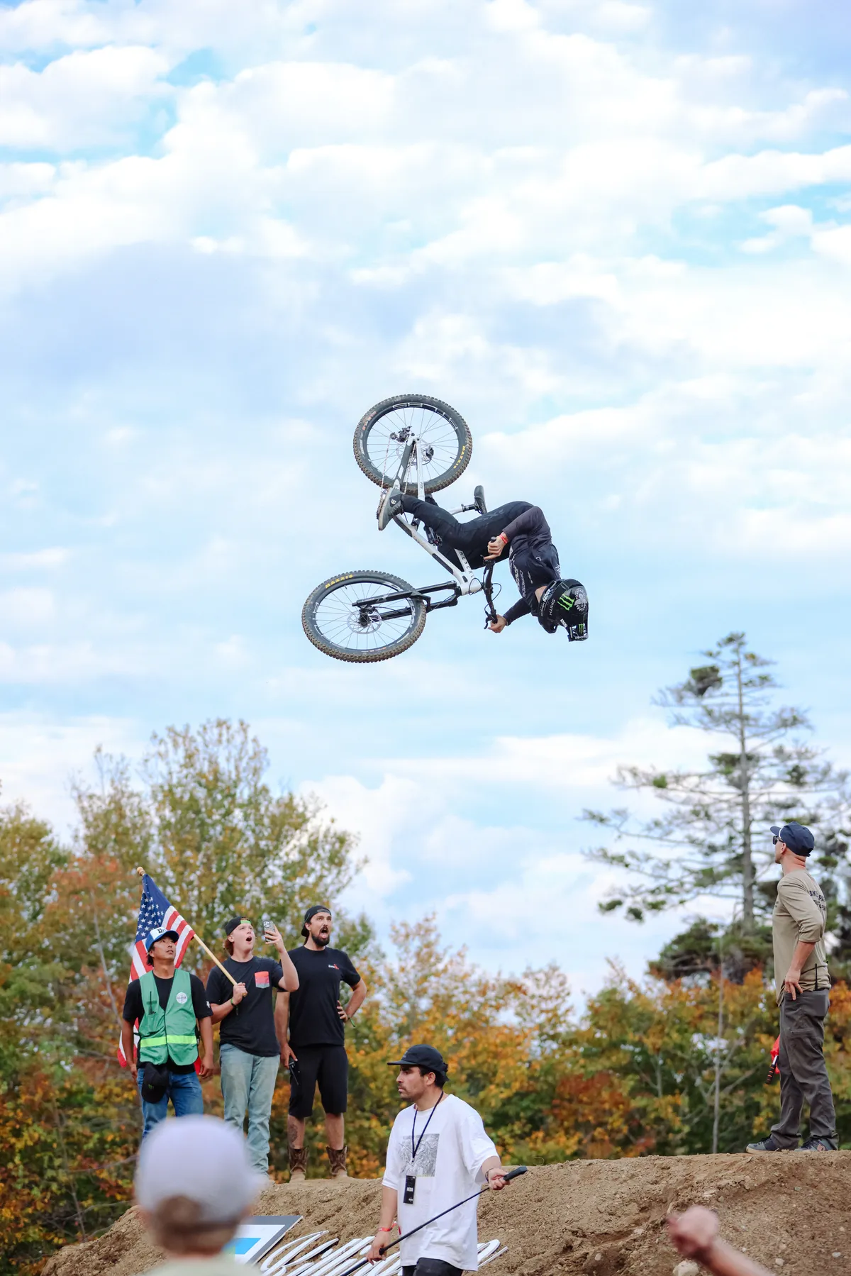 Mountain biker upside down in a backflip above fans waving an American flag on the hillside