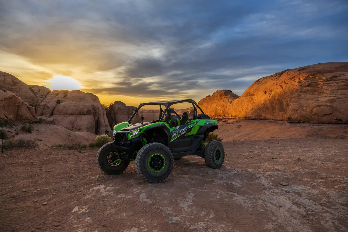 Green side-by-side parked on slickrock under a fiery sunset sky in Moab