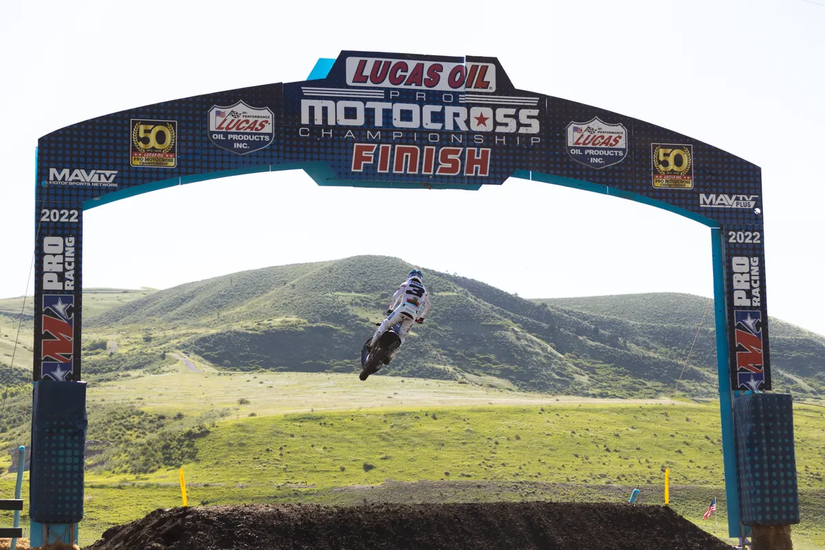 Tomac flying through the air beneath the finish arch at Thunder Valley with green hills behind