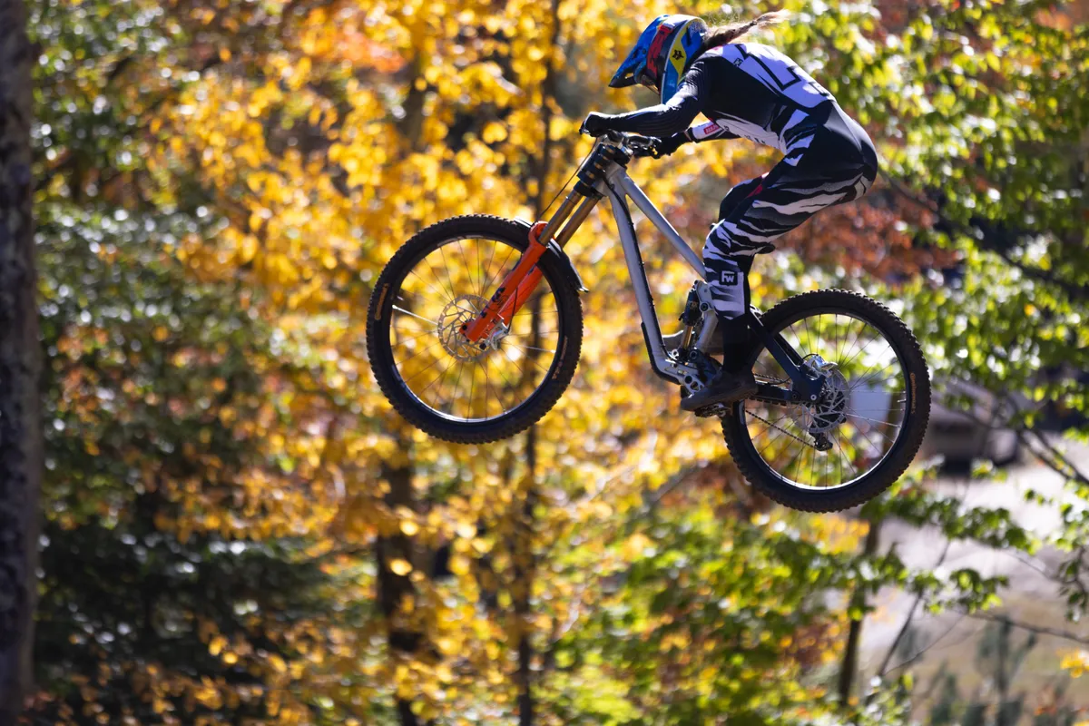 Downhill mountain biker flying through the air against a wall of bright autumn leaves