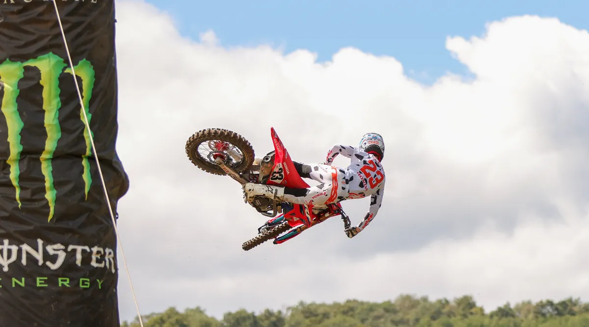 Motocross rider whipping his Honda sideways past a giant Monster Energy can against a cloudy sky, at Unadilla