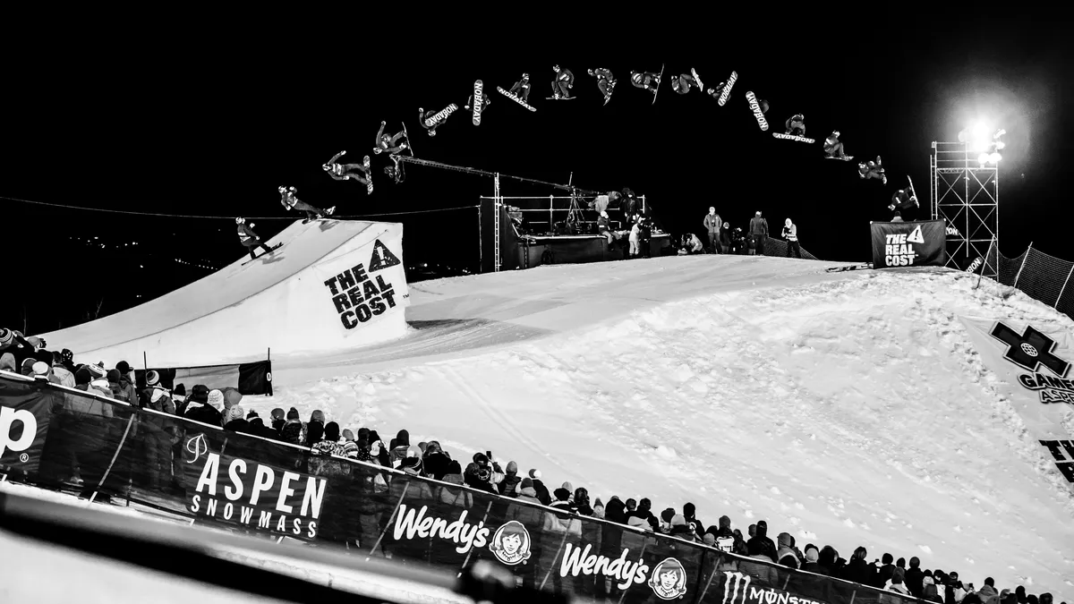 Sequence of a rider spinning off the floodlit big air jump at night above the crowd at X Games Aspen, in black and white