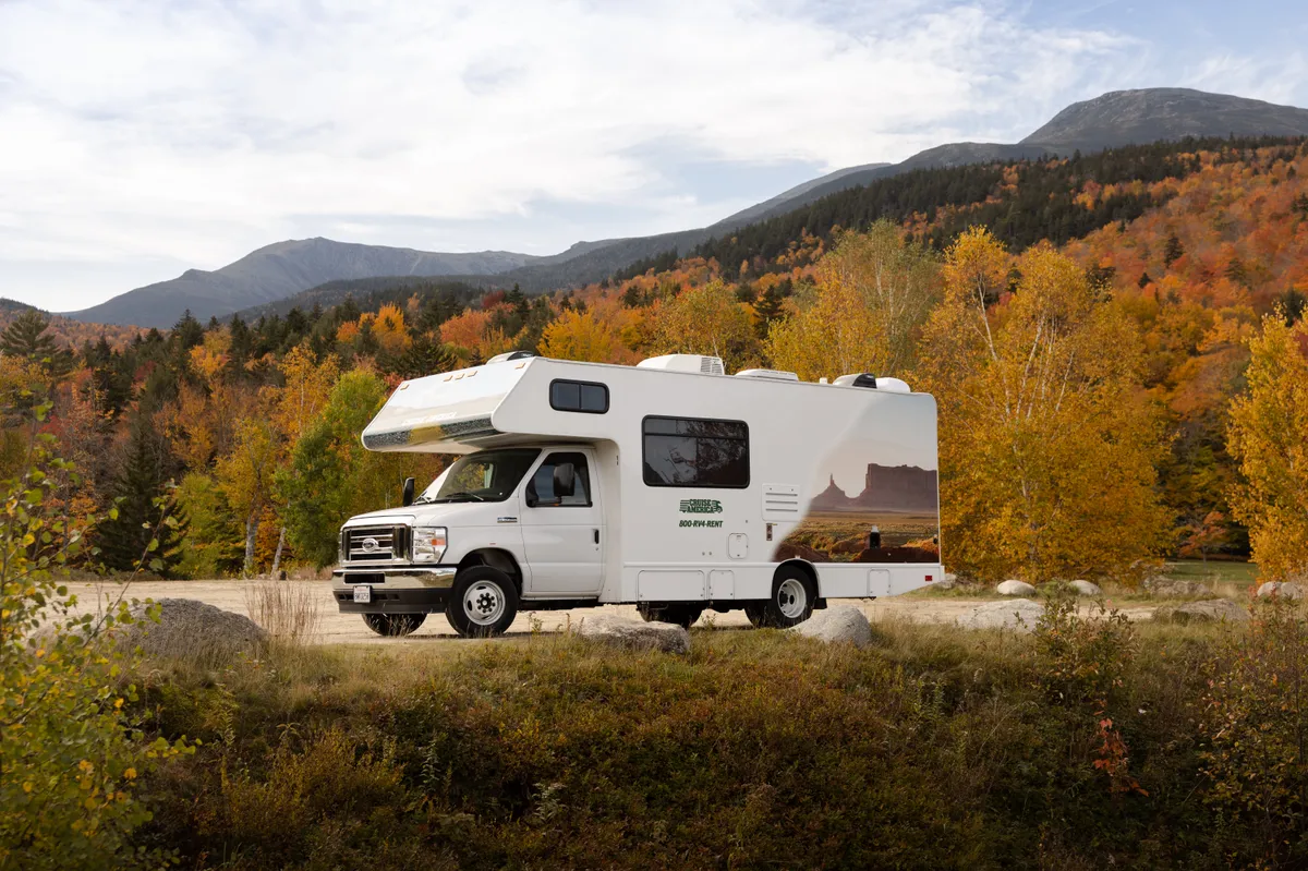 Class C motorhome parked in fall foliage below rounded mountains