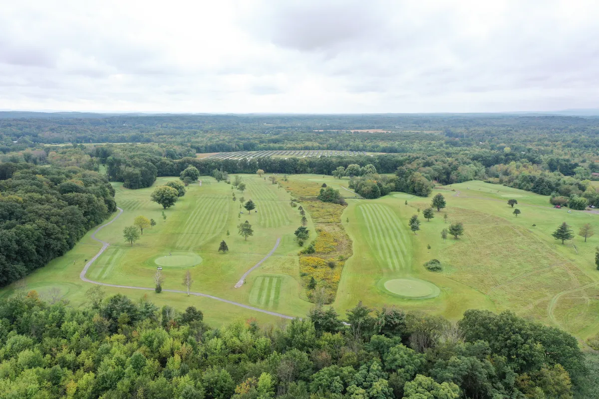 Aerial view of a tree-lined golf course with striped fairways and rolling countryside beyond