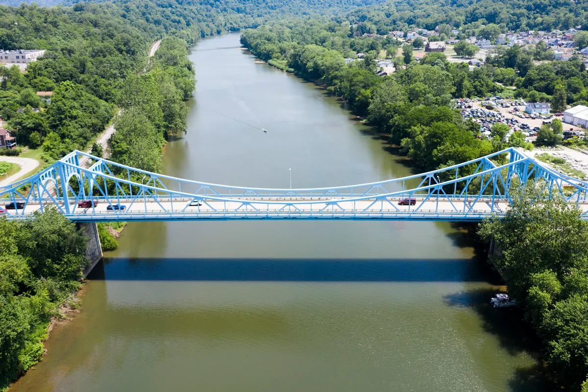 Drone view of a light-blue bridge over a wide river with the town on the banks