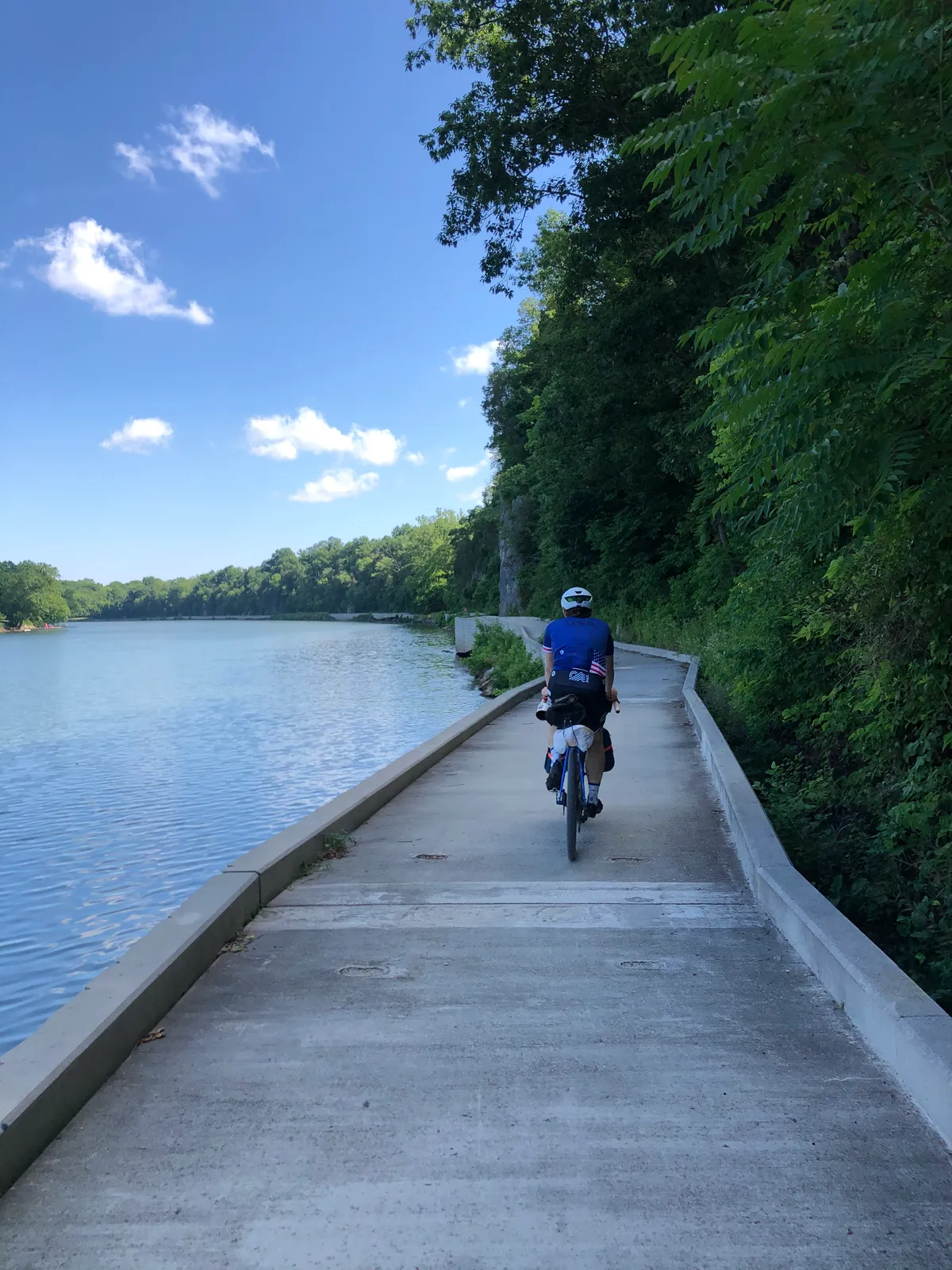 Dan riding a concrete boardwalk section along the wide Potomac under blue sky