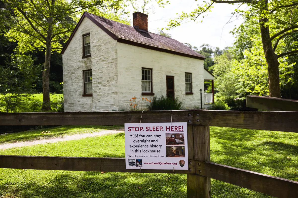 Whitewashed stone lockhouse with a Canal Quarters sign on the fence inviting visitors to stay overnight