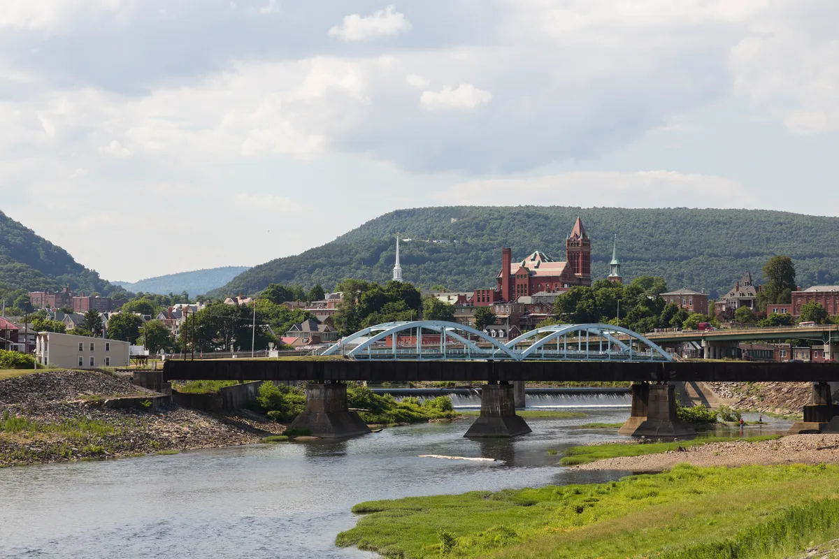 Blue truss bridges over the river in Cumberland, Maryland, with church spires and the town behind