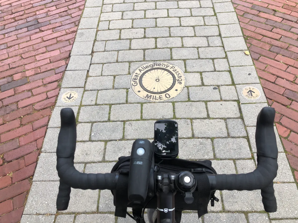 Looking over the handlebars at the Great Allegheny Passage Mile 0 medallion in the brick plaza in Cumberland