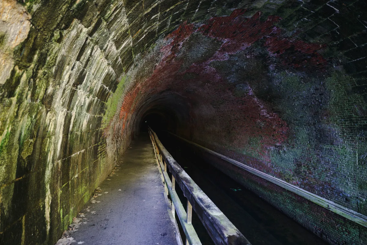 Inside the Paw Paw tunnel, brick walls in red and green tones with a railing along the towpath