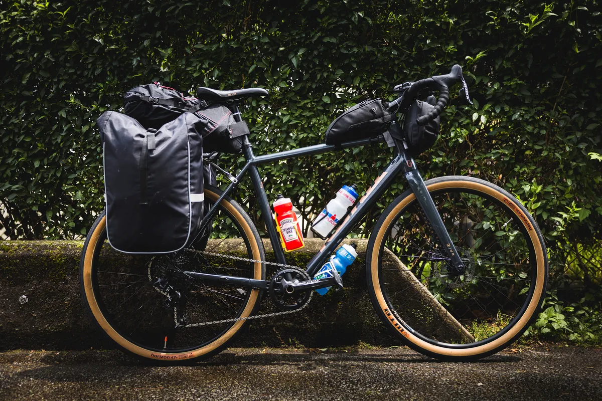 Grey Kona Rove gravel bike loaded with bags, side-on against greenery