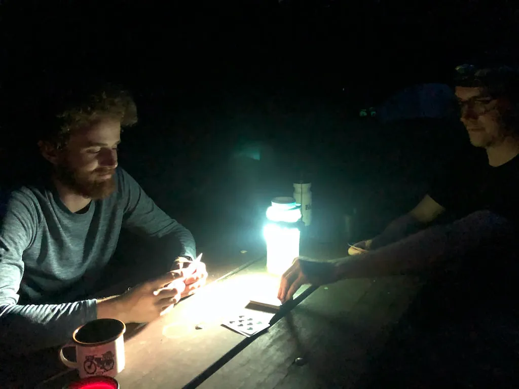Alex and Dan playing cards at night by lantern light at a picnic table