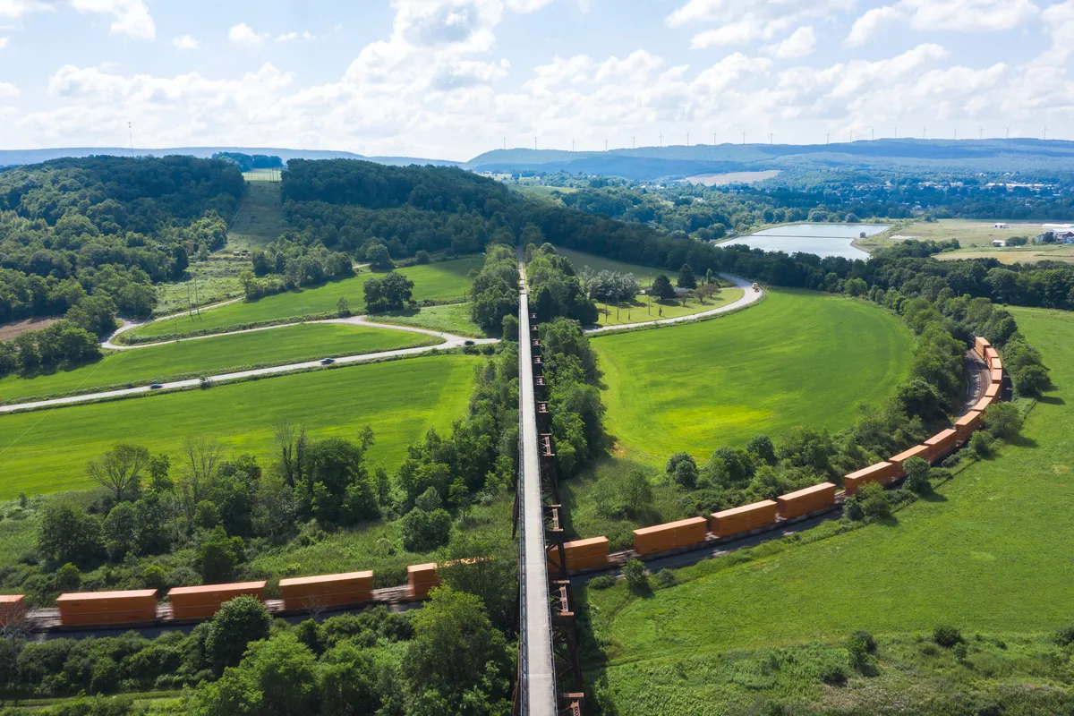 Drone view of the Salisbury Viaduct cutting across green fields with an orange freight train curving below
