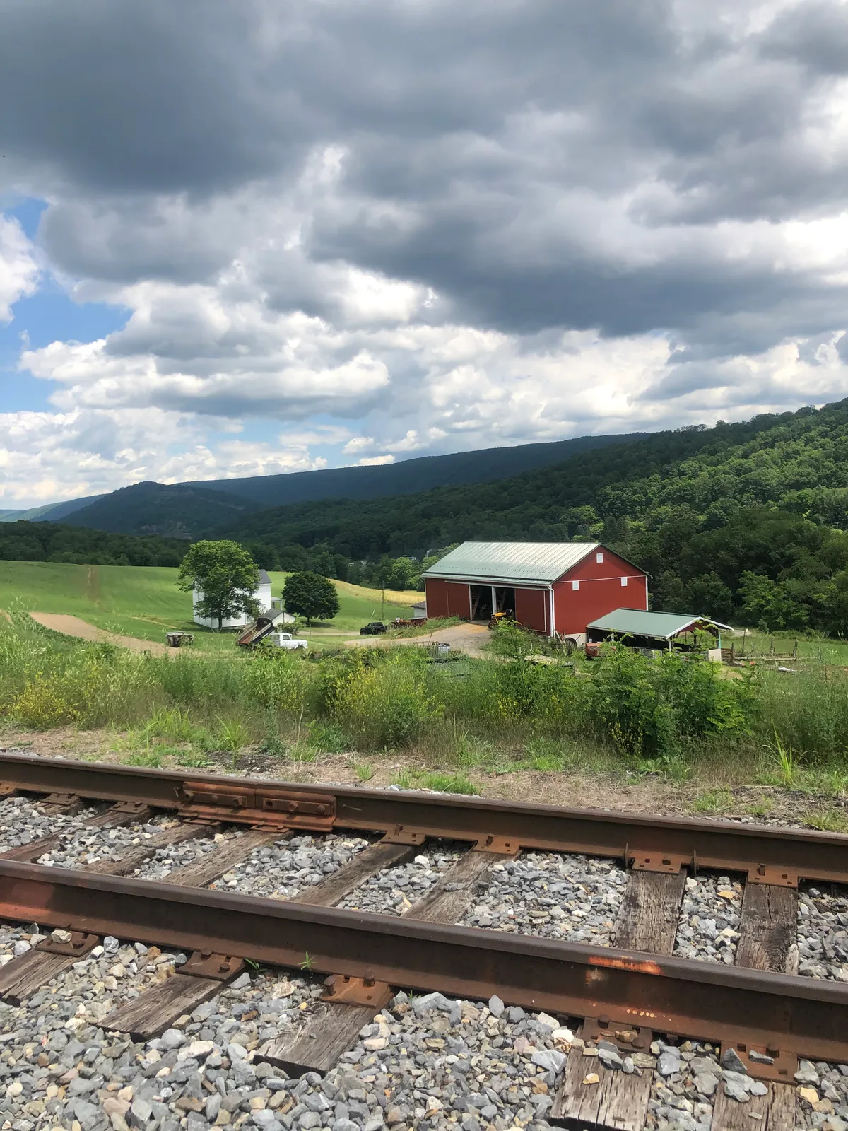 Railroad tracks in the foreground with a red barn and farm in the valley below