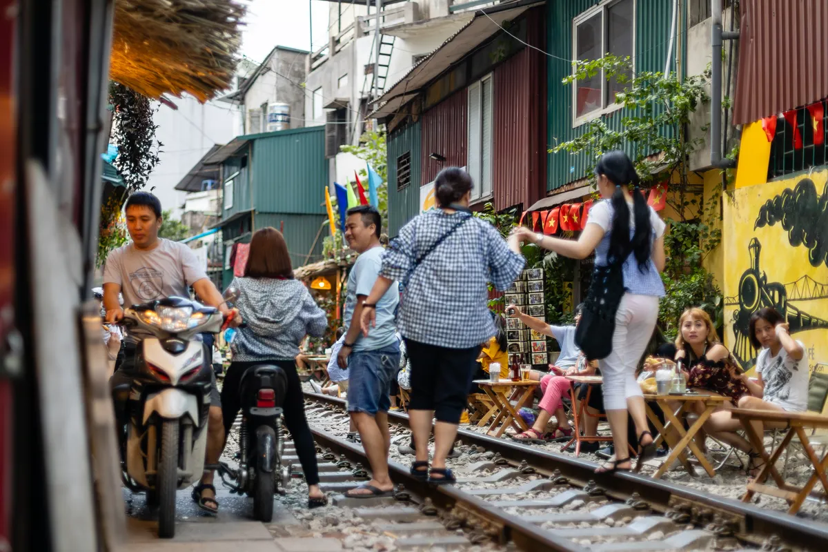 Tourists walking along the tracks past trackside cafe tables