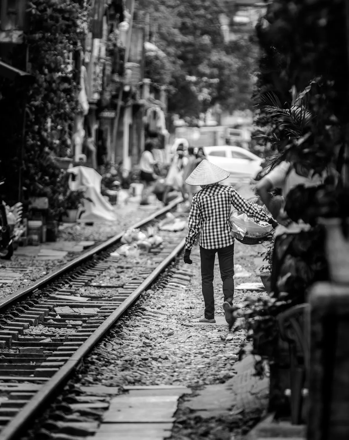 Black and white photo of a woman in a conical hat walking the tracks
