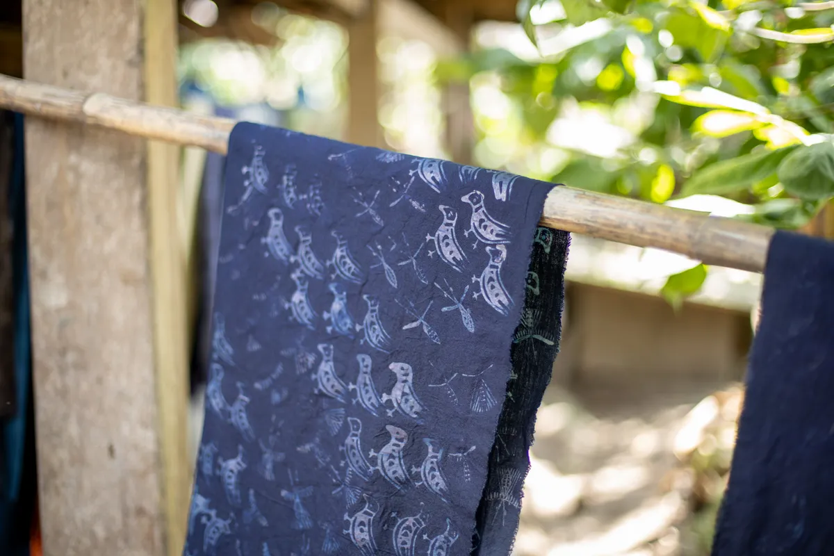 Indigo cloth with a white bird pattern drying over a bamboo pole