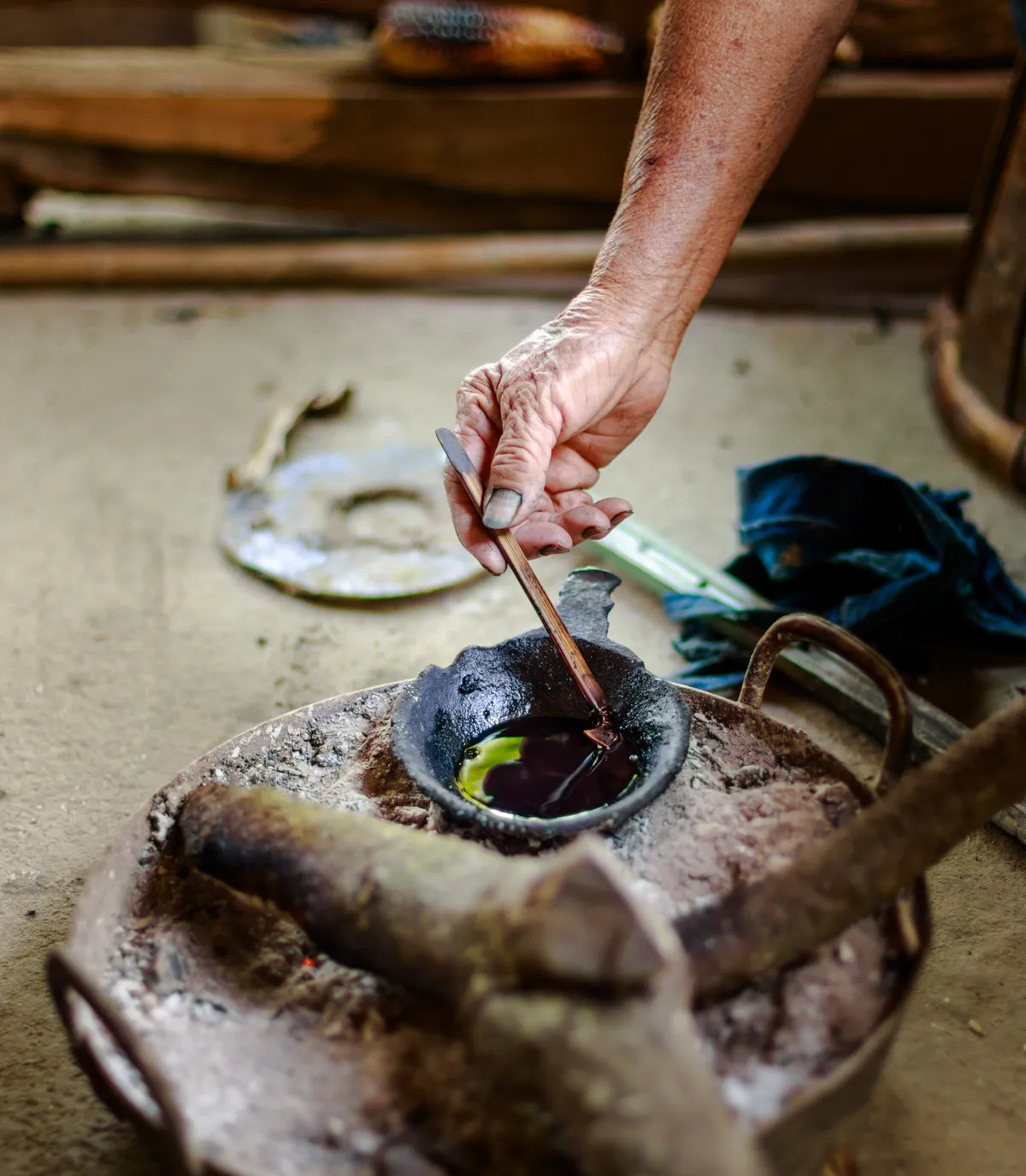 Hand stirring a small pot of dye over hot coals