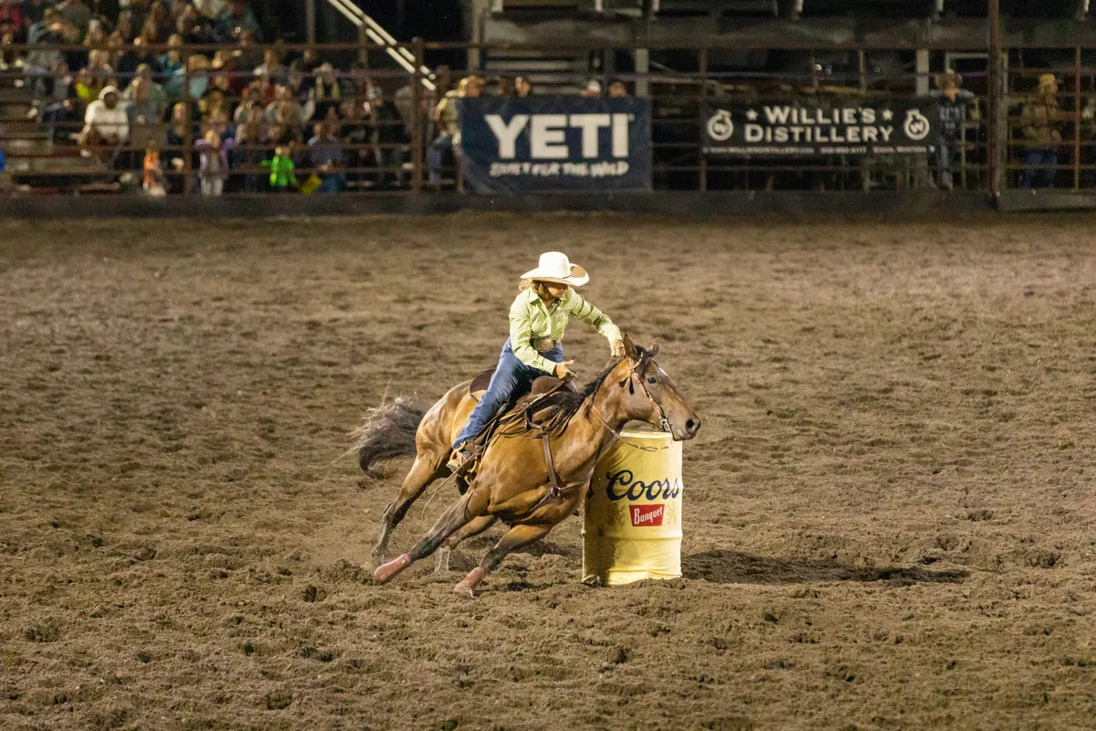 Barrel racer leaning her horse tight around a barrel under the arena lights