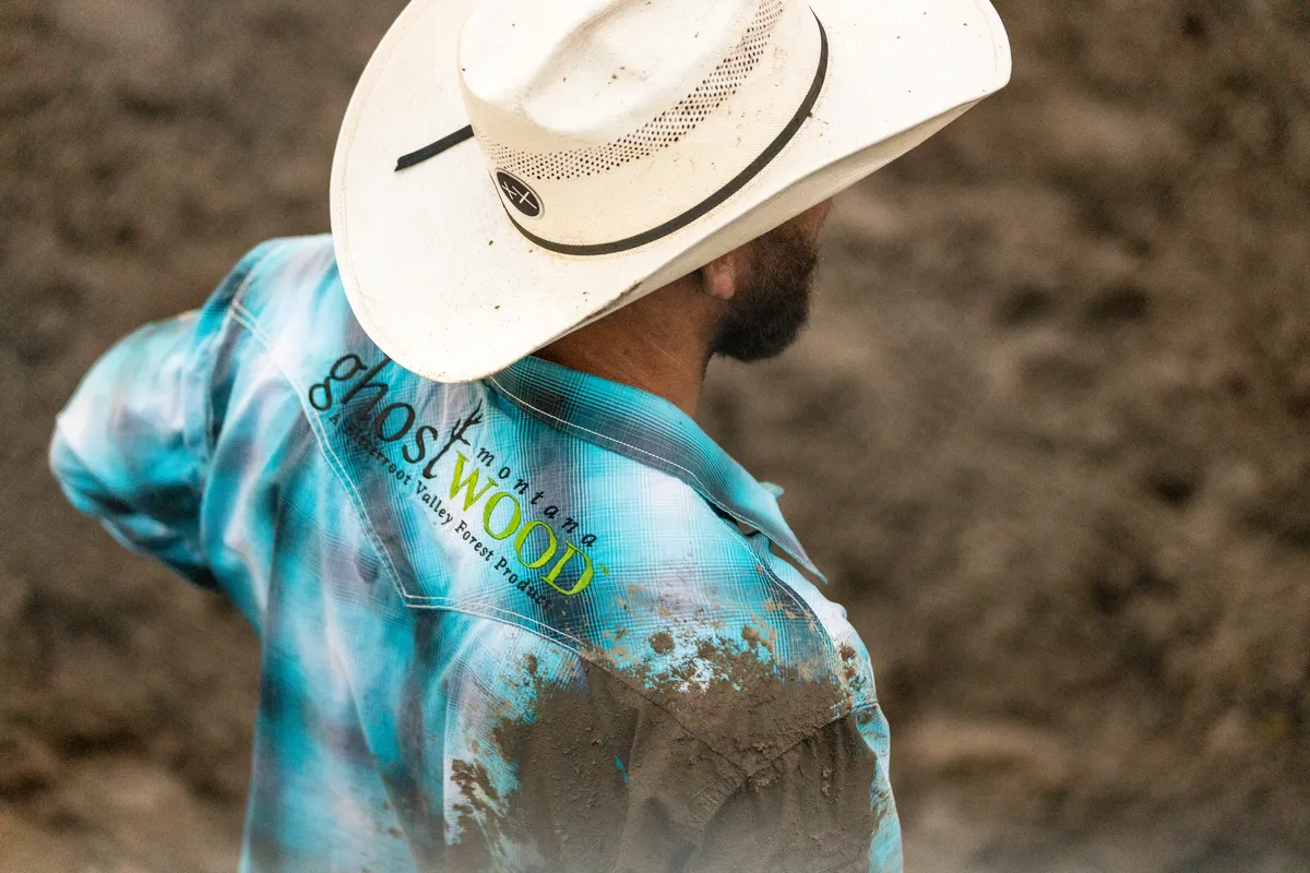 Cowboy in a white straw hat and mud-splashed turquoise shirt seen from behind