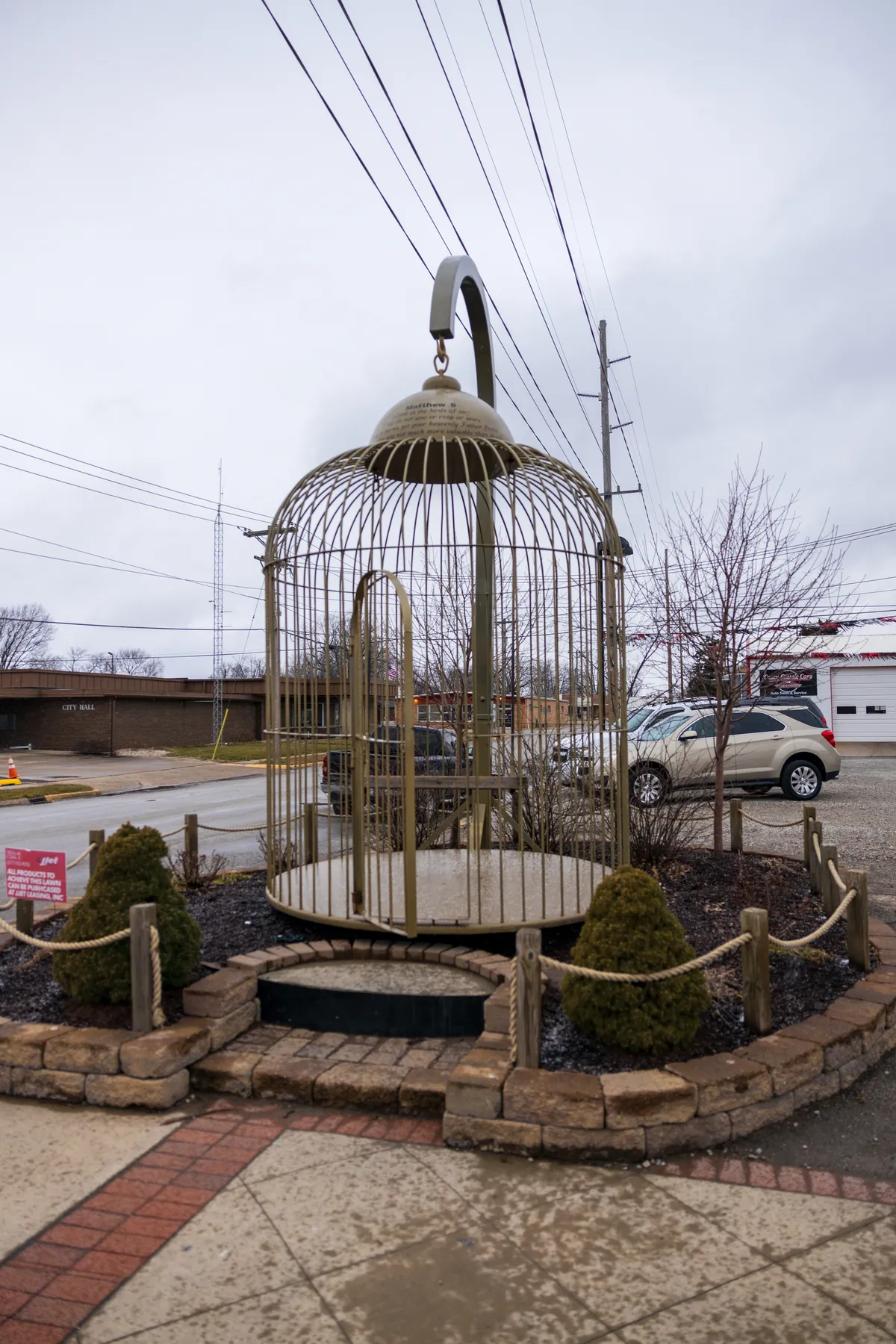 Giant birdcage on a street corner with a car parked behind it