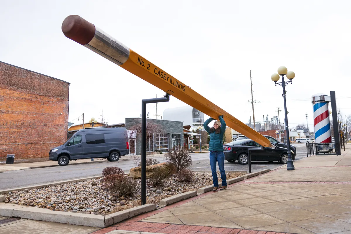 Visitor holding up the end of a giant yellow pencil on a downtown sidewalk