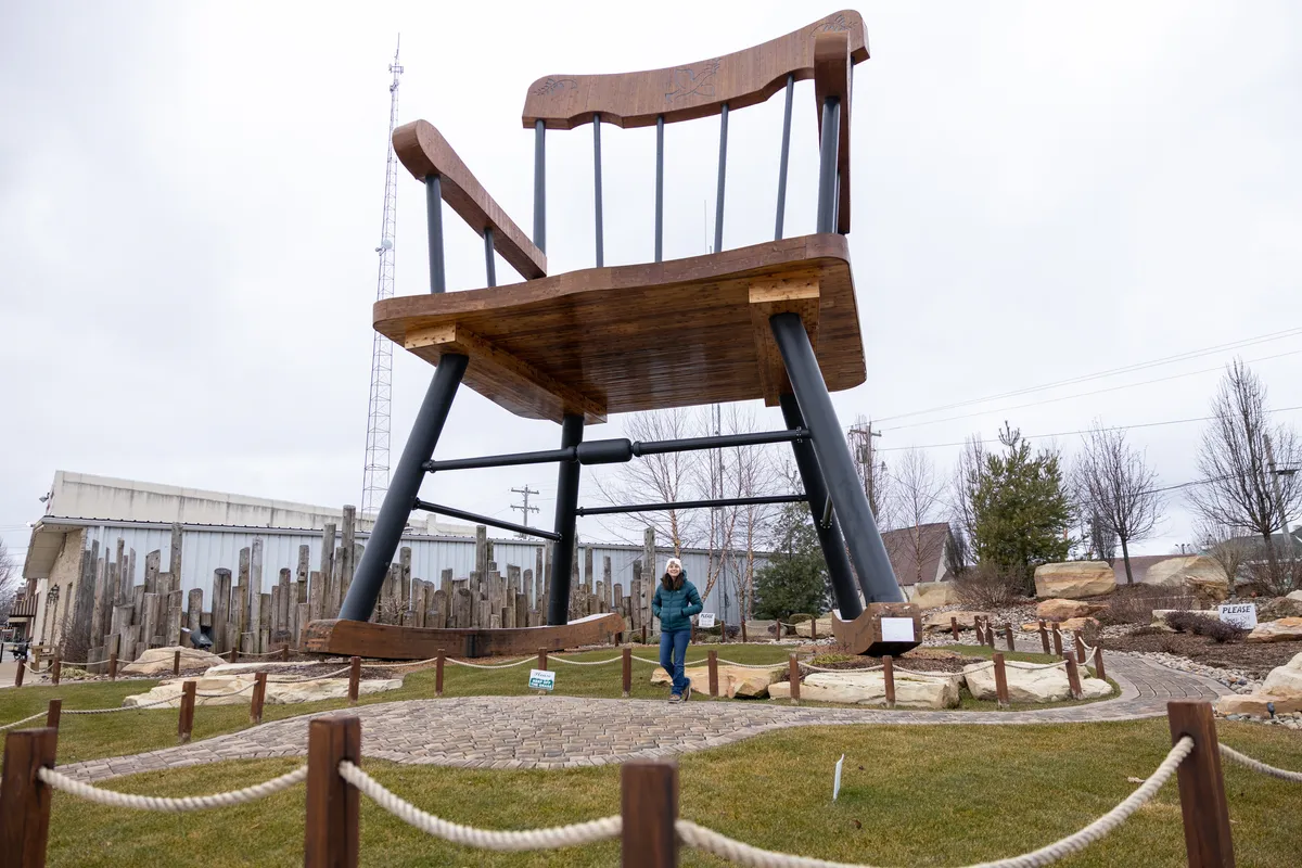 Giant wooden rocking chair with a person standing between its legs for scale