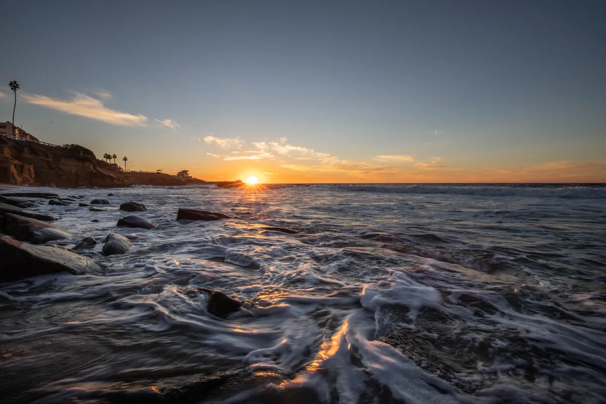Waves washing over rocks on the San Diego coast as the sun sets on the horizon