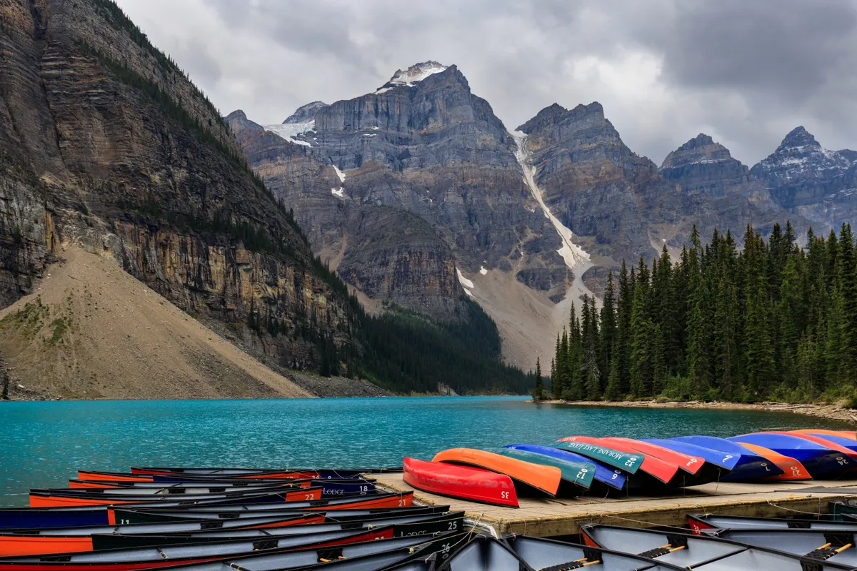 Rows of colourful canoes on a dock at turquoise Moraine Lake below jagged peaks