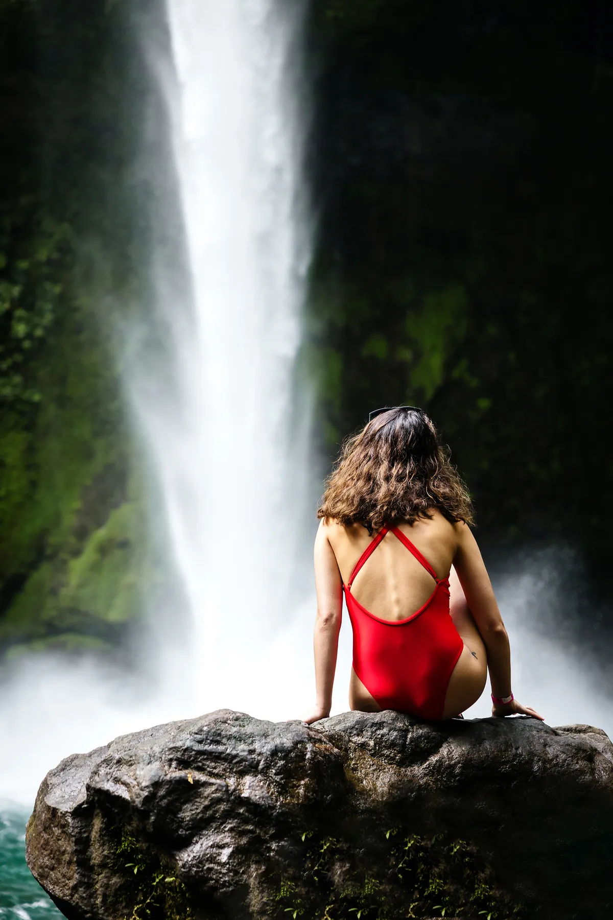 Woman in a red swimsuit sitting below a waterfall