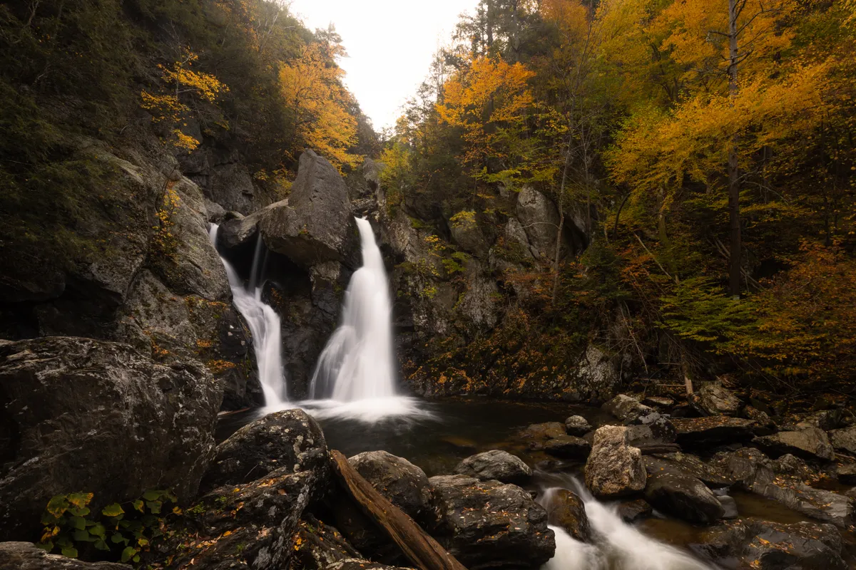 Bash Bish Falls splitting around a rock into a pool in an autumn gorge