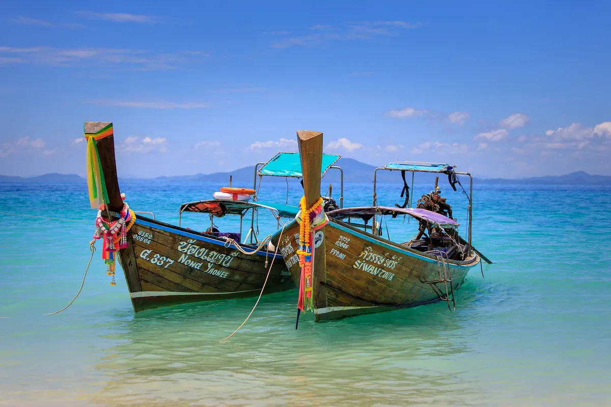 Two longtail boats decorated with garlands moored in turquoise water off Bamboo Island