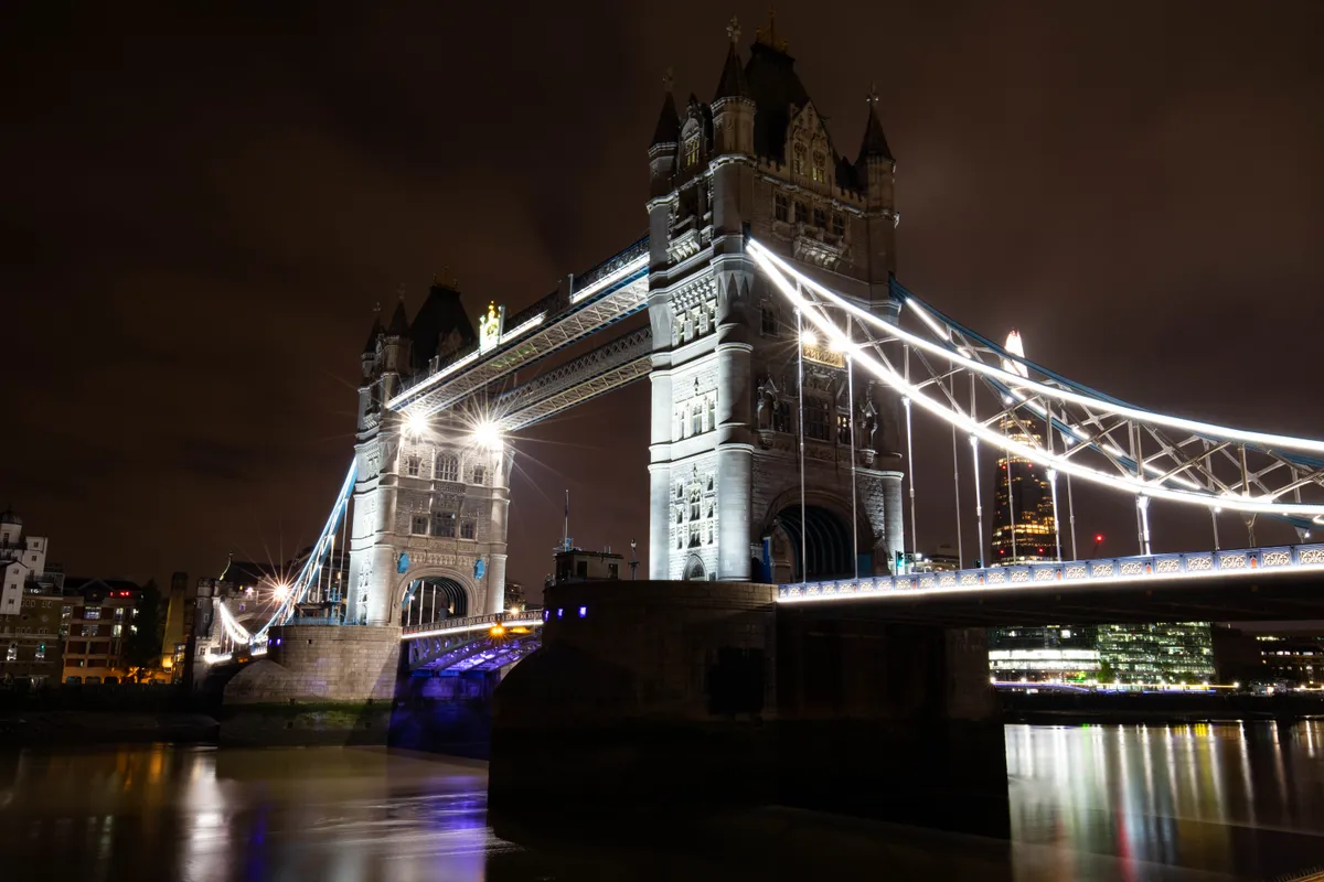 Tower Bridge lit up at night with its reflection in the Thames
